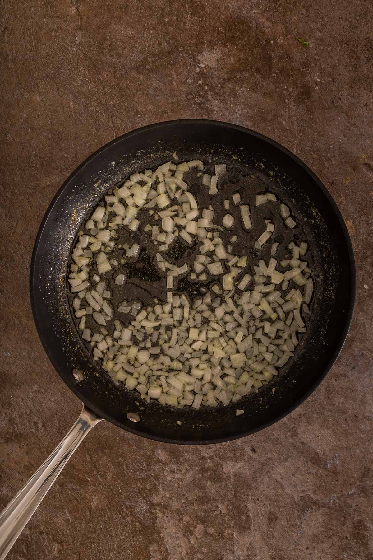 Chopped onions cooking in a black frying pan on a brown textured surface, perfect for adding savory flavor to your favorite sheet pan pancakes or trying alongside a classic sheetpan pancake recipe.