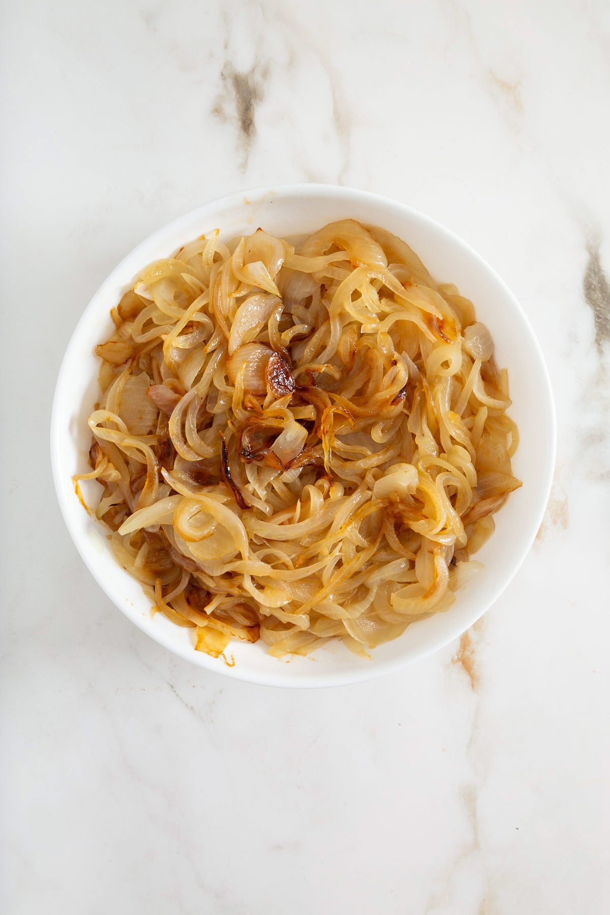 White bowl filled with caramelized onions on a white marble surface-perfect as a delicious topping for easy sheetpan pancakes or savory sheet pan pancakes from mix.
