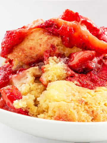 A serving of strawberry cobbler with a golden, crumbly topping and baked strawberries in a white bowl, reminiscent of an easy strawberry spoon cake recipe.