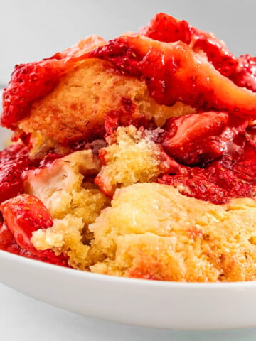 A close-up of a bowl of strawberry cobbler with golden biscuit topping and baked strawberries, reminiscent of the beloved strawberry spoon cake recipe featured in NYT.