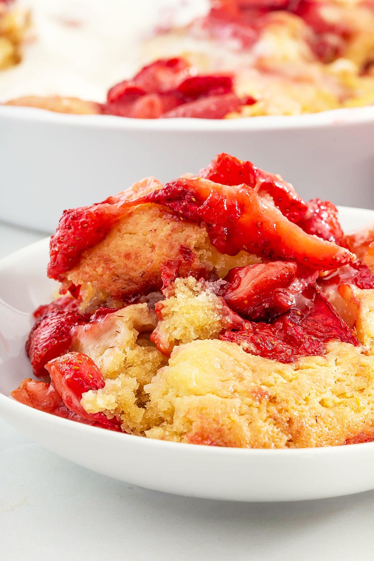 A close-up of a serving of strawberry cobbler with golden cake topping and juicy strawberries on a white plate, reminiscent of the flavors in an easy sheetpan pancake recipe.