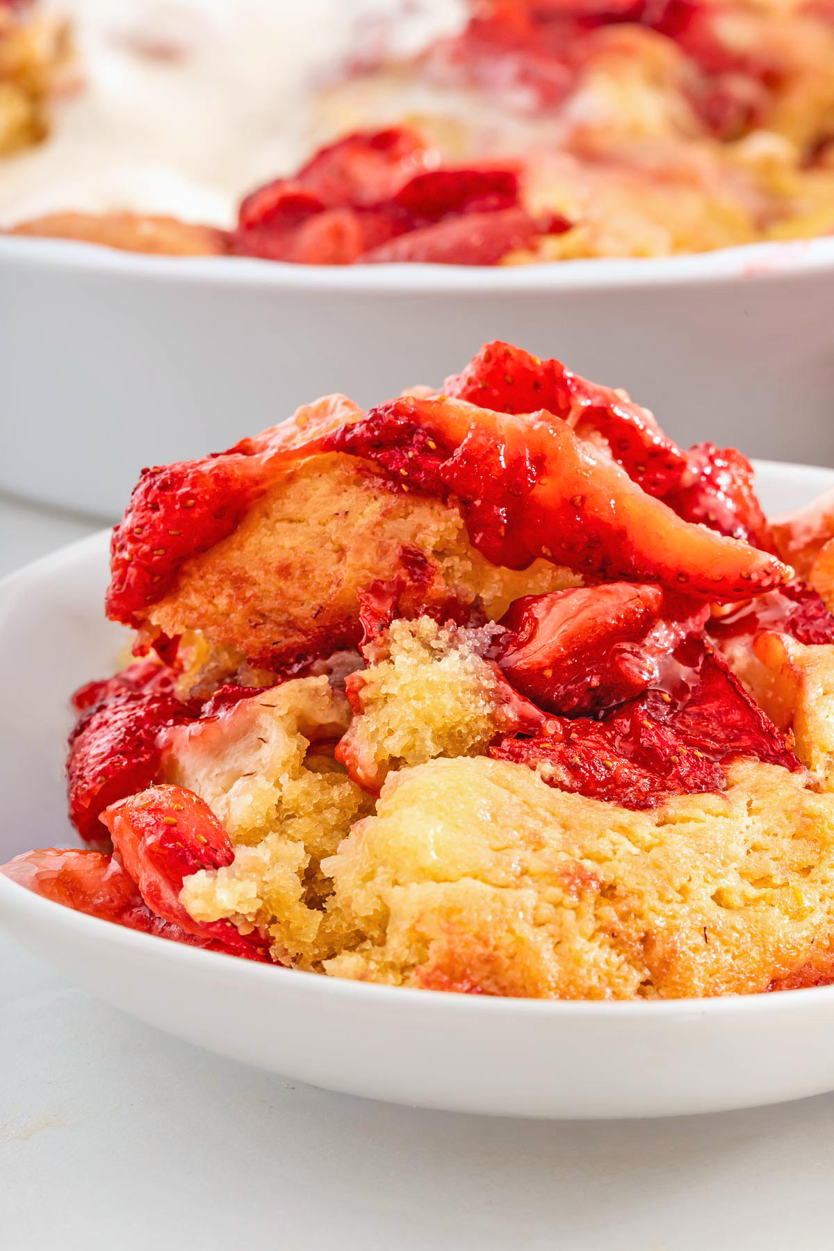A close-up of a serving of strawberry spoon cake, featuring chunks of baked strawberries and golden crust on a white plate, reminiscent of an easy strawberry spoon cake from NYT.