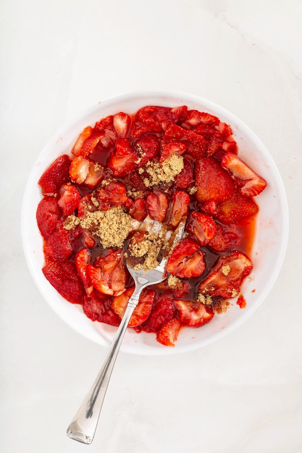 A white bowl filled with sliced strawberries, brown sugar sprinkled on top, and a silver spoon resting inside-perfect as a fresh topping for your sheet pan pancakes from mix.
