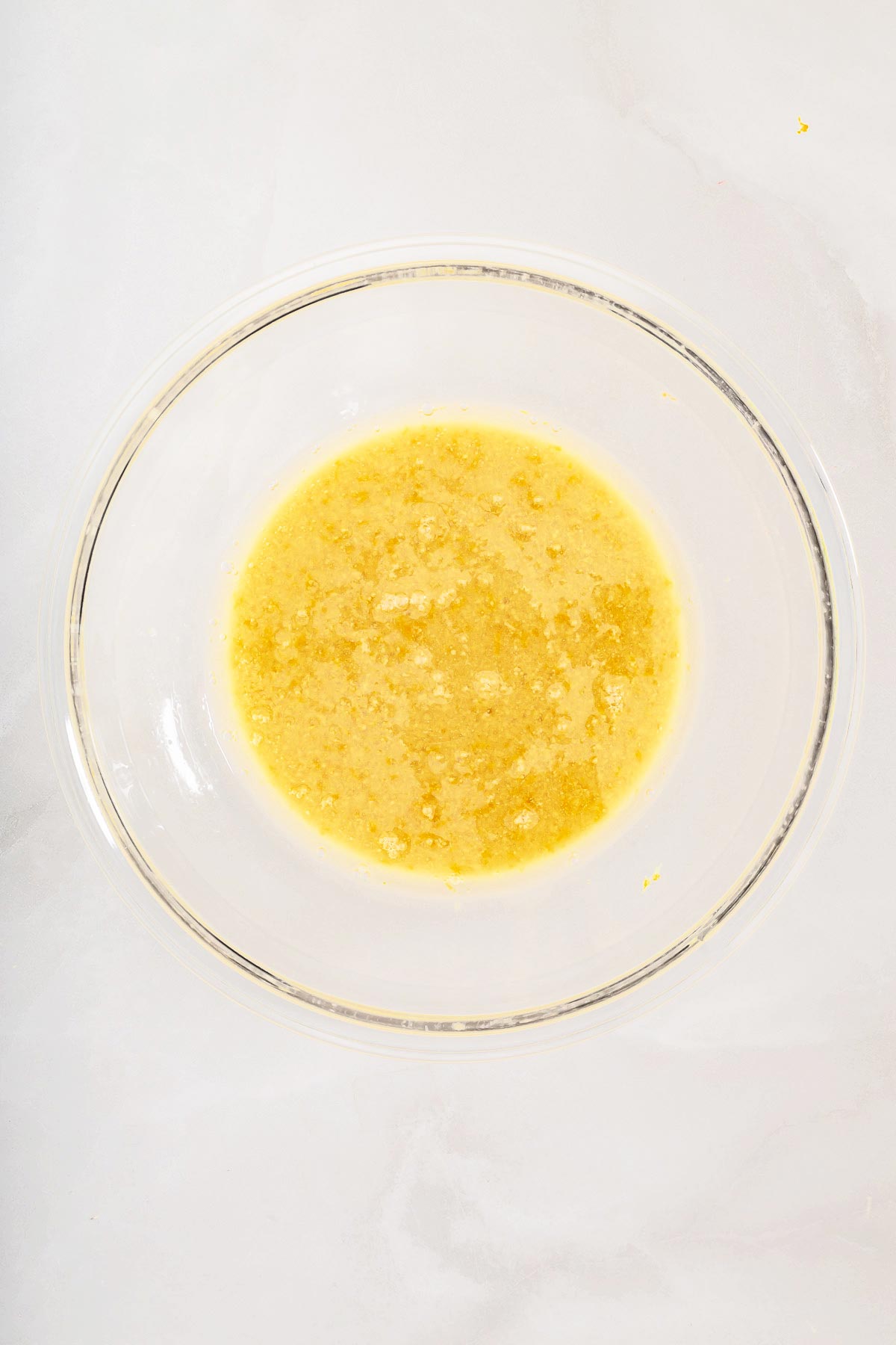 Clear glass bowl containing a mixture of melted butter and sugar on a light-colored surface, perfect for starting your easy sheetpan pancakes.