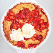 Baked strawberry cobbler topped with two scoops of vanilla ice cream in a white dish, photographed from above—a delicious treat that shares the comforting, crowd-pleasing appeal of classic sheet pan pancakes.
