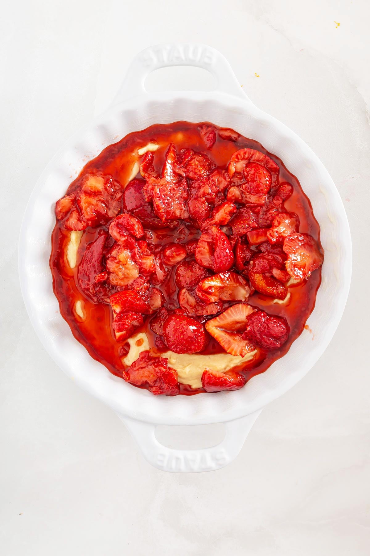 White baking dish filled with strawberry pie filling and sauce over an unbaked pie crust, viewed from above on a light surface-perfect inspiration for those who love easy sheetpan pancakes and other simple, crowd-pleasing desserts.