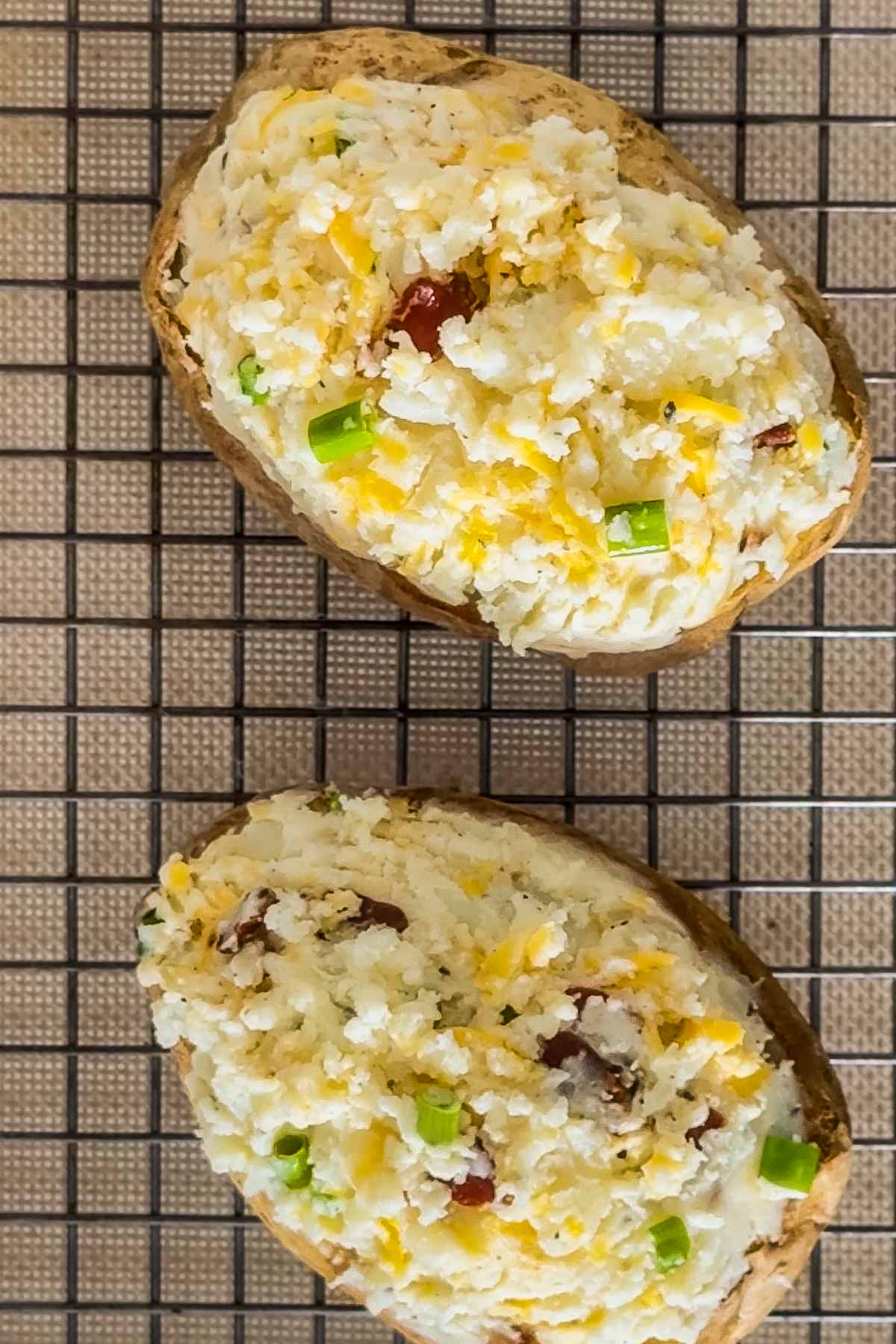 Two twice-baked potato halves with cheese, bacon bits, and green onions on a cooling rack-perfect to serve alongside a fresh batch of easy sheetpan pancakes for a hearty breakfast spread.