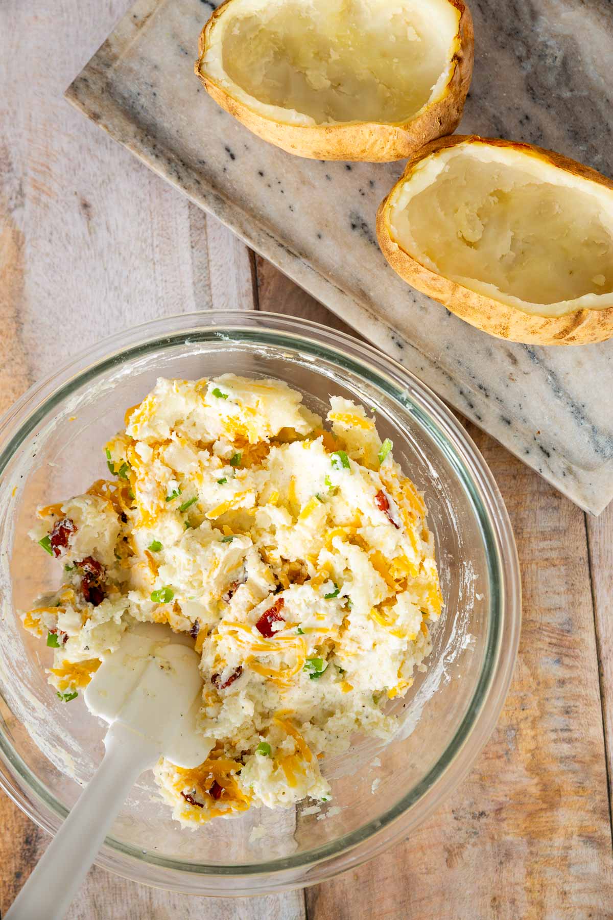 A glass bowl filled with a mashed potato mixture next to two empty baked potato skins on a wooden surface, reminiscent of the effortless preparation found in a sheetpan pancake recipe.