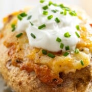 Close-up of a baked potato topped with melted cheese, sour cream, and chopped chives on a decorative plate—perfect comfort food to pair with easy sheetpan pancakes for a hearty meal.
