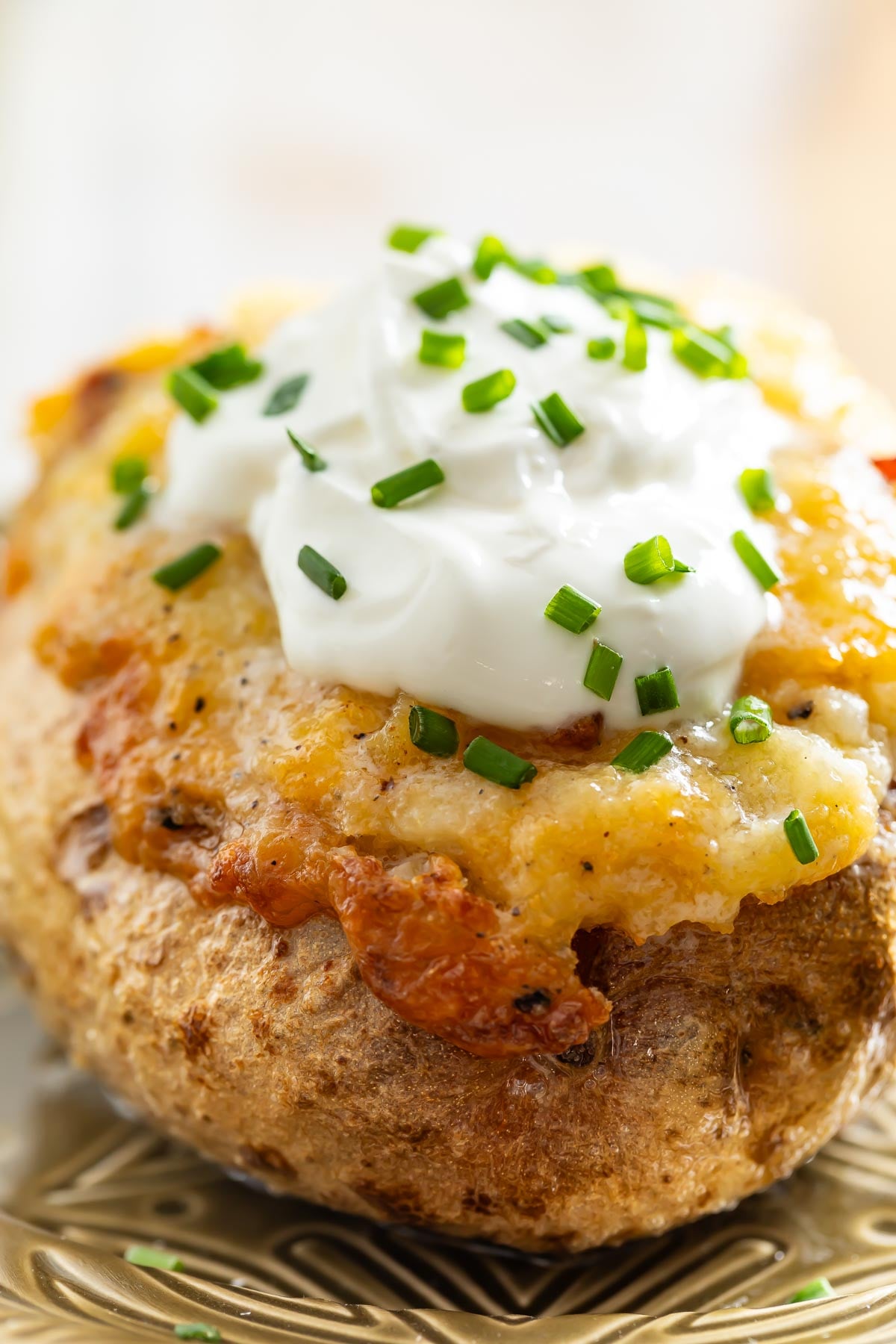 Close-up of a baked potato topped with melted cheese, sour cream, and chopped chives on a decorative plate—perfect comfort food to pair with easy sheetpan pancakes for a hearty meal.