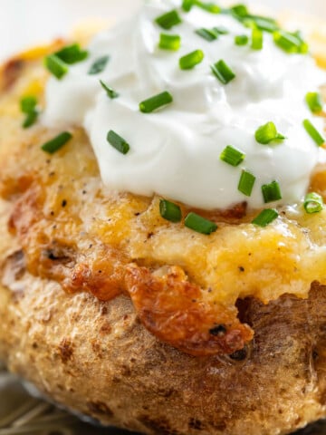 Baked potato topped with melted cheese, sour cream, and chopped chives on a plate-delicious comfort food that's just as satisfying and simple to prepare as easy sheetpan pancakes.