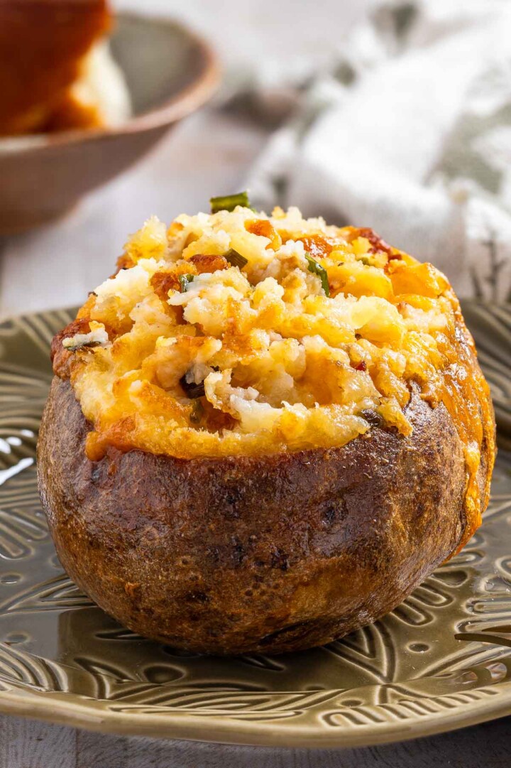A baked potato with melted cheese and breadcrumbs on top sits on a patterned plate, making it look just like a classic recipe for twice baked potatoes.