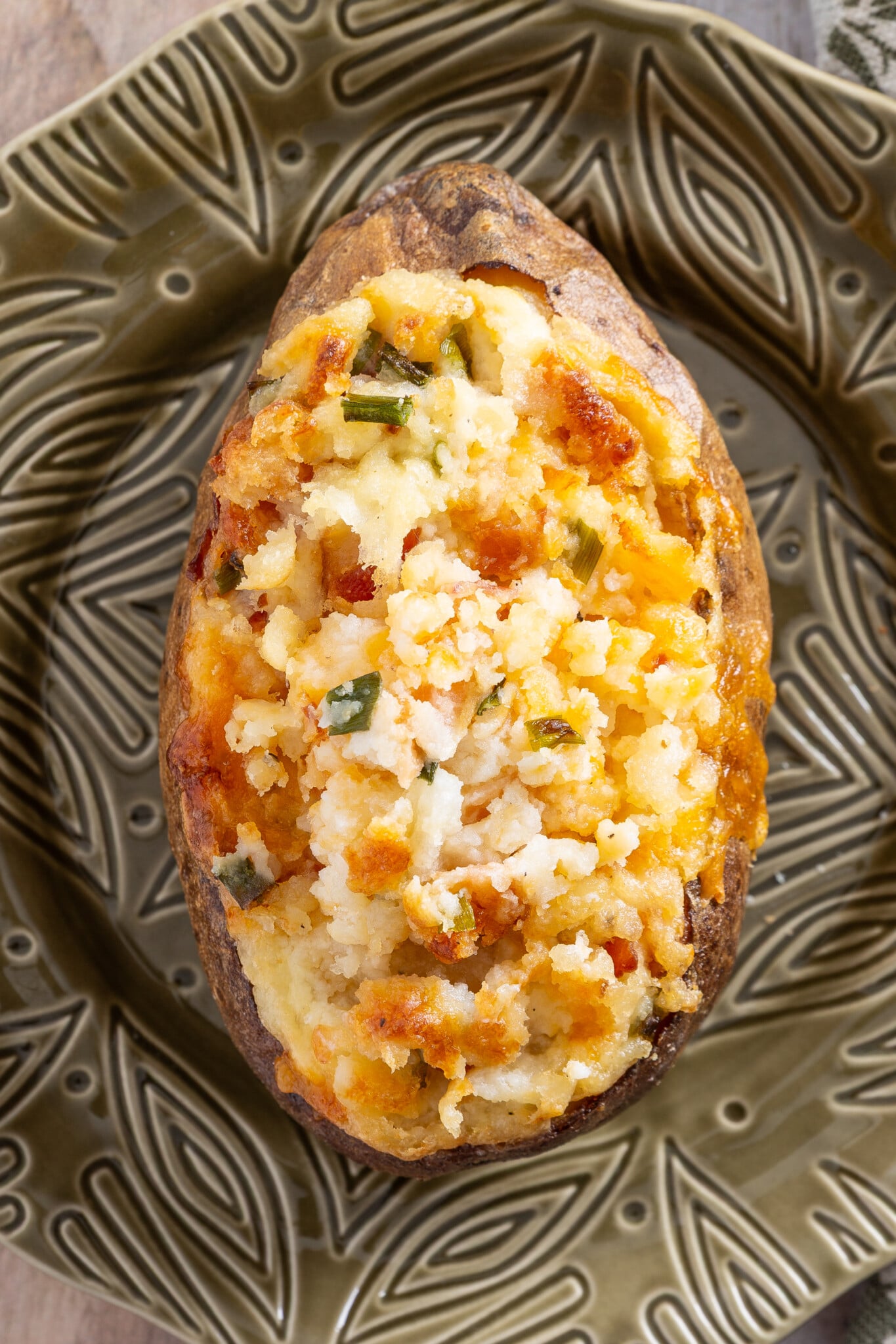 A twice-baked potato topped with melted cheese and chopped green onions sits on a decorative green plate, showcasing the best twice baked potato recipe for an irresistible side dish.