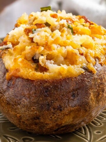 A baked potato with a crispy skin, filled with mashed potatoes, melted cheese, and chopped green herbs, is served on a decorative plate-a delicious twist inspired by the best twice baked potato recipe.