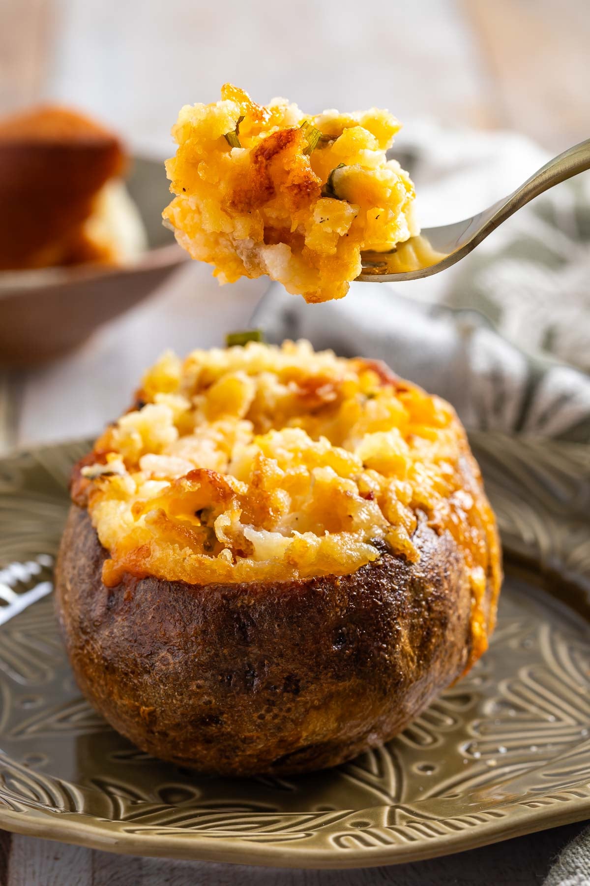 A baked potato with a crispy skin is filled with a cheesy, golden mashed potato mixture; a fork is lifting a bite above the potato—perfect inspiration for the best twice baked potato recipe.