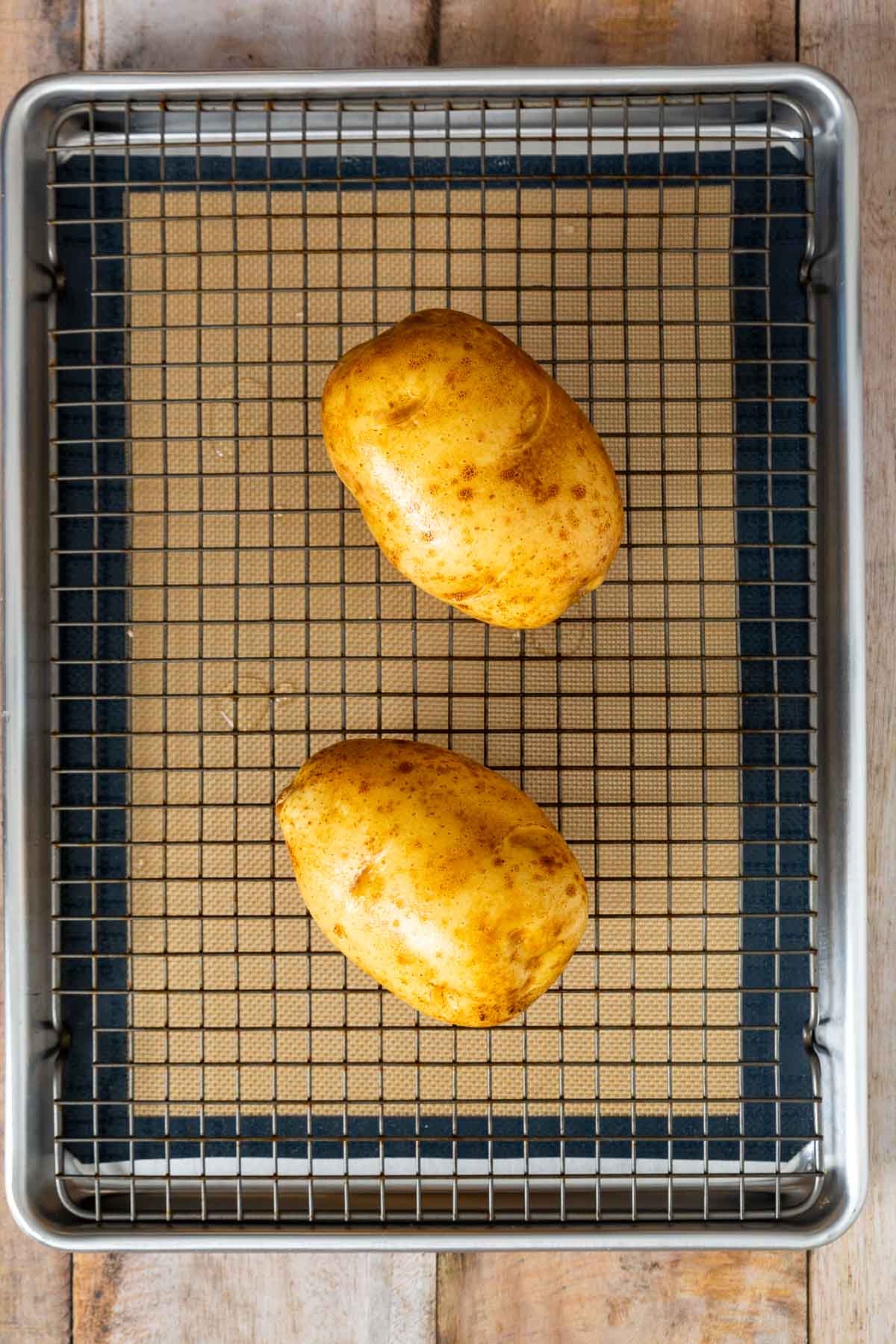 Two whole russet potatoes on a wire rack set over a baking sheet lined with a silicone mat, just like preparing your favorite sheetpan pancake recipe or those easy sheet pan pancakes from mix.