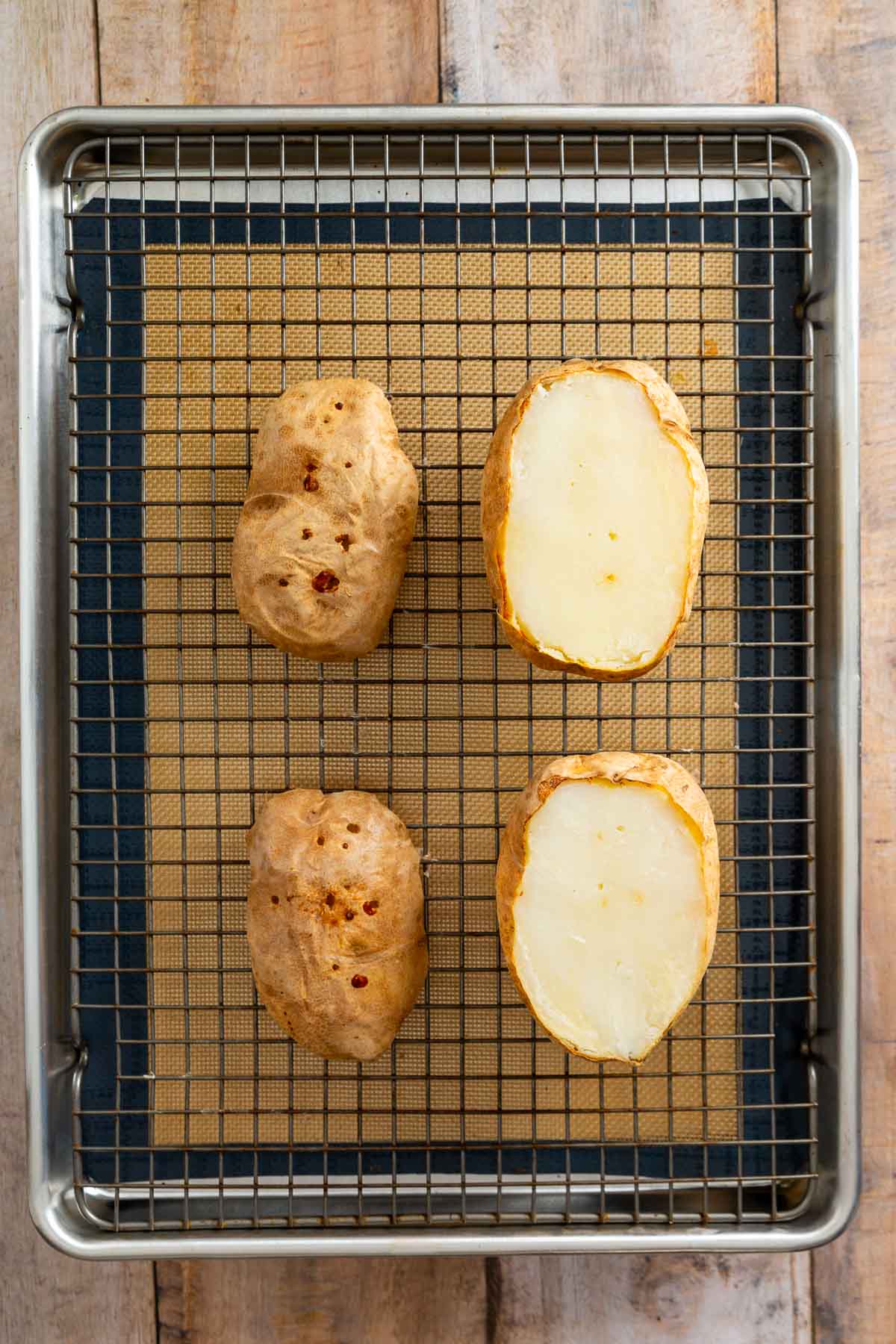 Two whole baked potatoes and two potato halves are arranged on a wire rack over a baking sheet lined with a silicone mat, ready to share oven space with an easy sheetpan pancake recipe for a convenient, crowd-pleasing breakfast.
