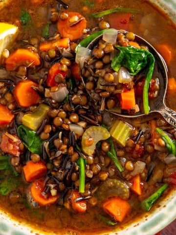 A bowl of lentil and wild rice soup with carrots, celery, and spinach, served with a side lemon wedge, is the perfect savory alternative to sheet pan pancakes.