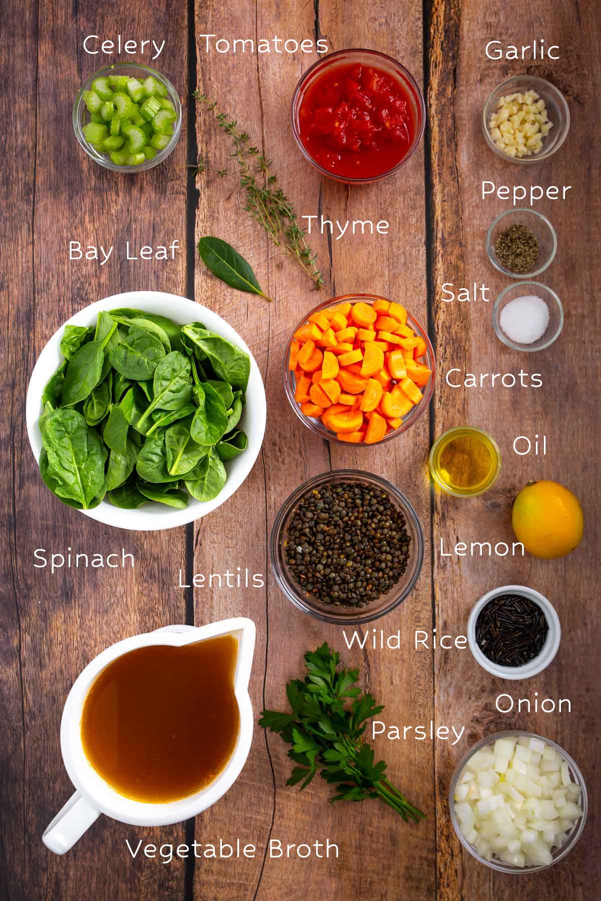 Labeled ingredients for soup, including spinach, lentils, broth, carrots, tomatoes, celery, onion, garlic, rice, oil, lemon, herbs, and spices, are arranged on a wooden table like an easy sheetpan pancake.