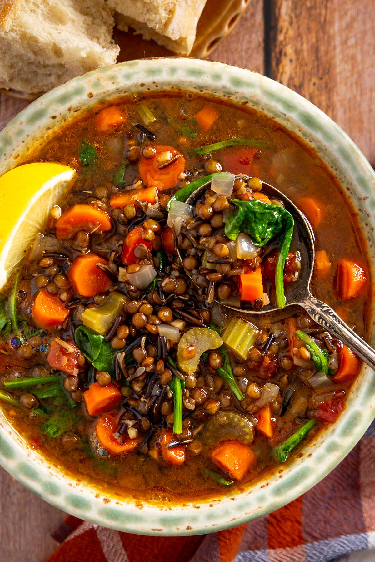 A bowl of lentil and wild rice soup with carrots, celery, and spinach, served with a spoon and a slice of lemon, perfect for enjoying alongside a sheetpan pancake.