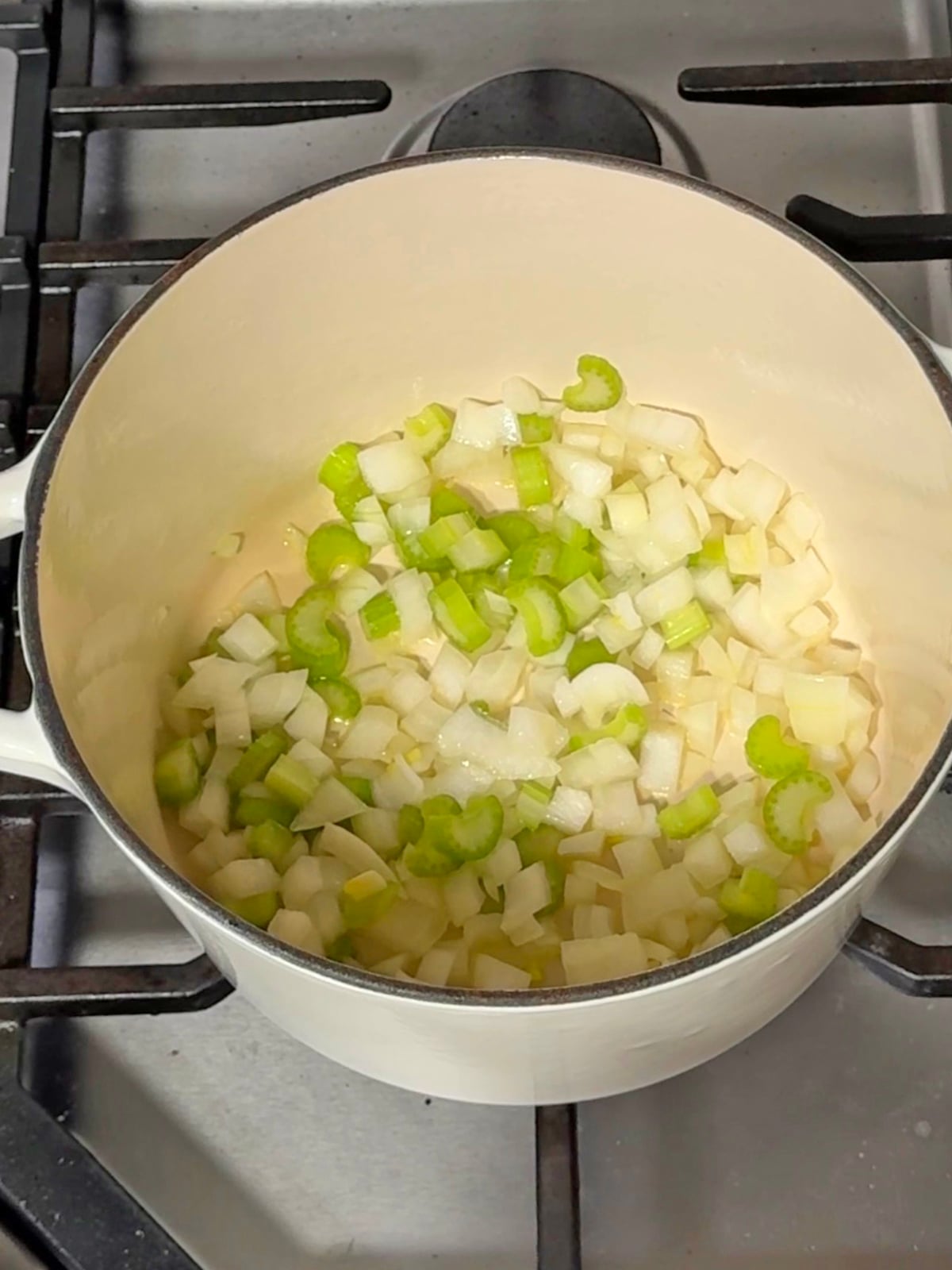 Diced onions and celery sautéing in a white pot, the base for a carrot and red lentil soup.