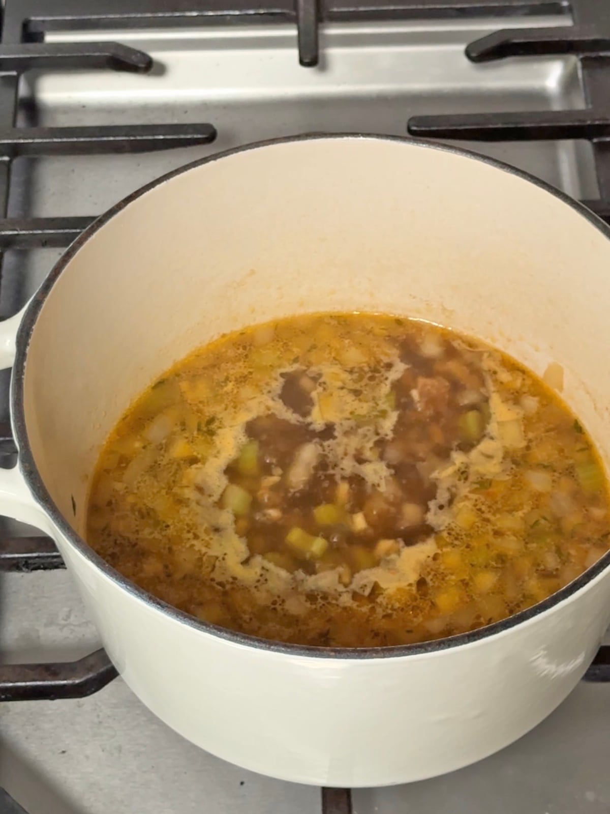 Carrot and red lentil soup simmering in a white enameled cast iron pot on a stovetop.