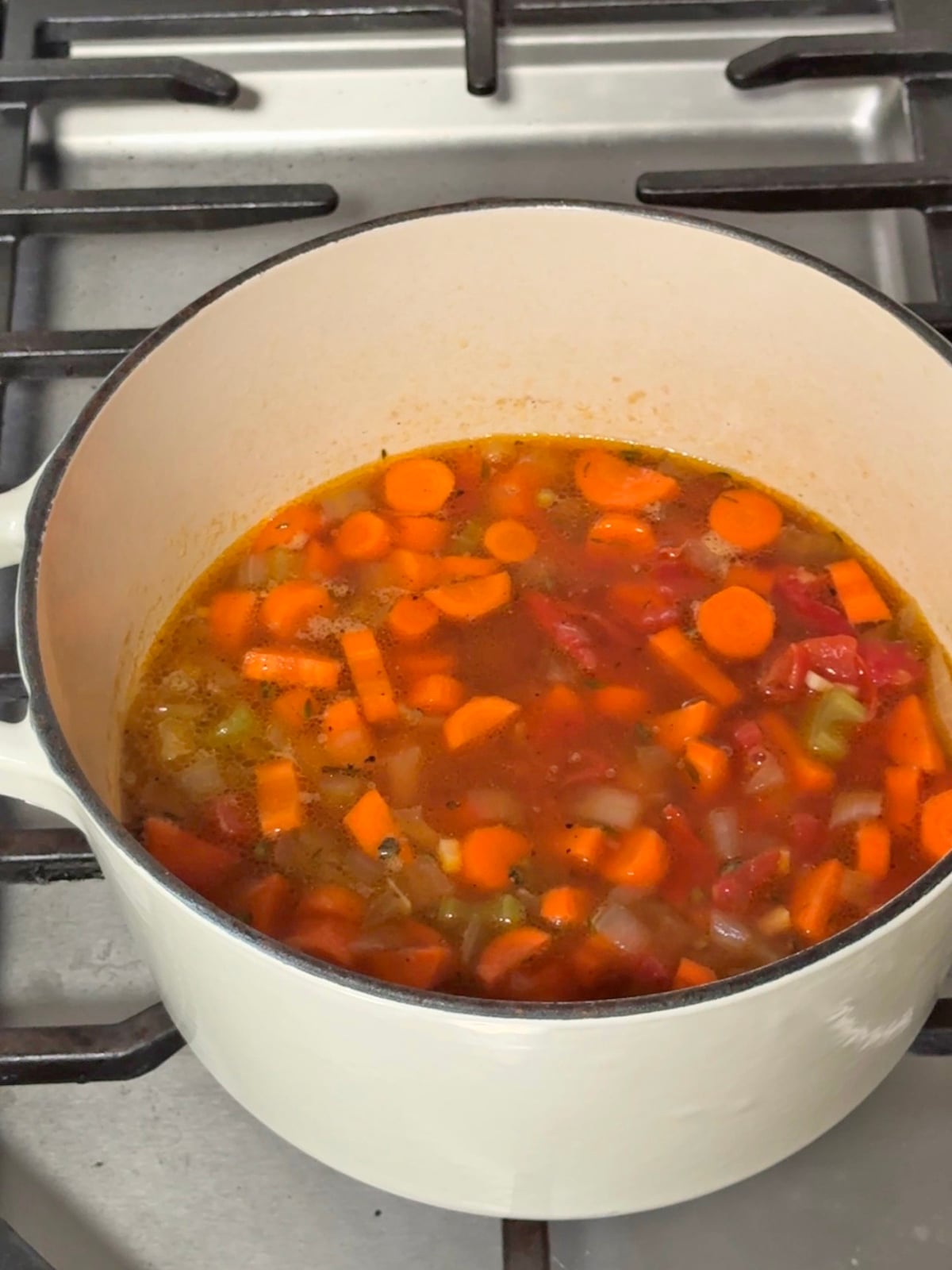 Carrot and red lentil soup simmering in a white enameled pot on a stovetop.